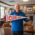 Man holding a 'Good Curling!' Felt pennant in a curling lounge