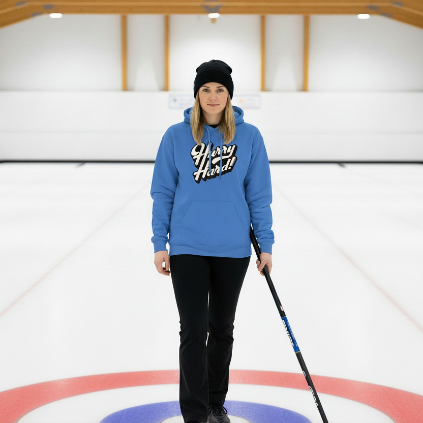 Person in a blue hoodie and black pants standing on a curling rink with a broom.